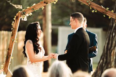 Couple exchanging vows under a wooden arch decorated with vines.
