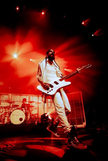 Musician passionately playing guitar on stage with vibrant red lighting.