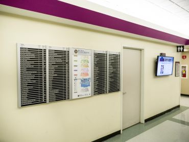 Hospital hallway with name boards and a screen.