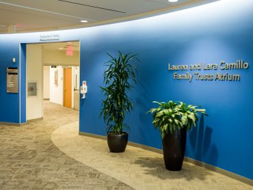 Blue hospital corridor with plants and signage.