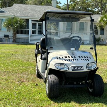 White golf cart with "Setwake Karts" sign parked on grass in front of a house.