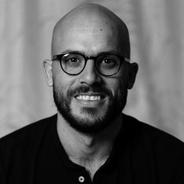 Portrait of a smiling bald man with glasses and a beard.