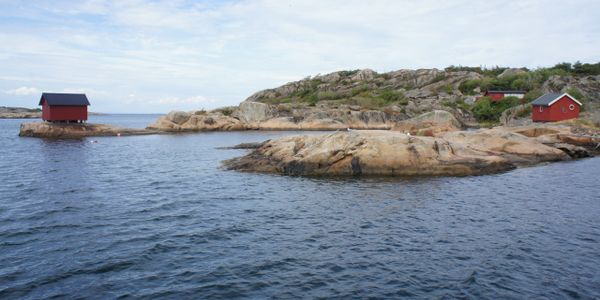 Red cabins on rocky islands by calm sea under cloudy sky.
