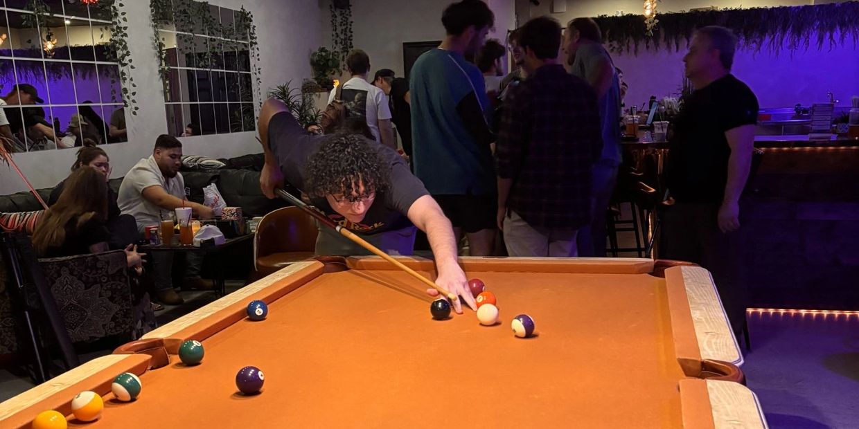 Young man focused on taking a shot in a lively indoor pool hall.