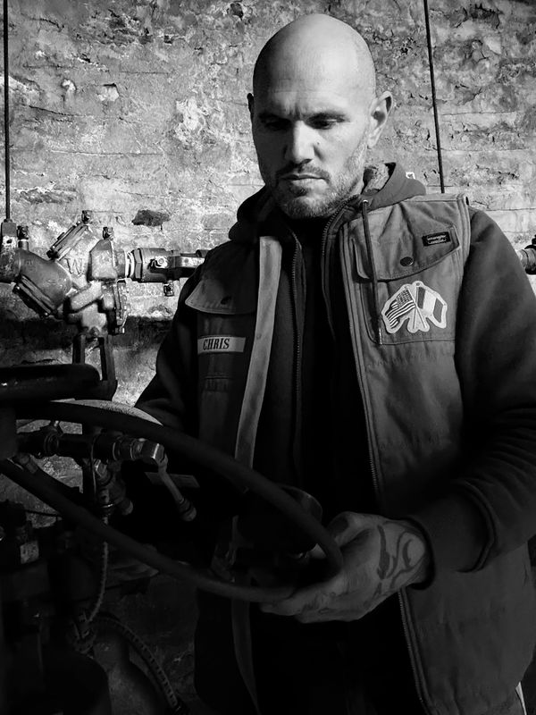 A man named Chris working with industrial pipes in a dimly lit space.