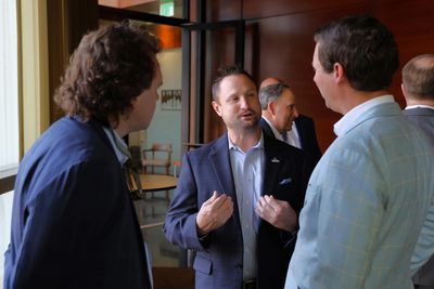 Three men in suits engaged in a conversation indoors at a professional event.