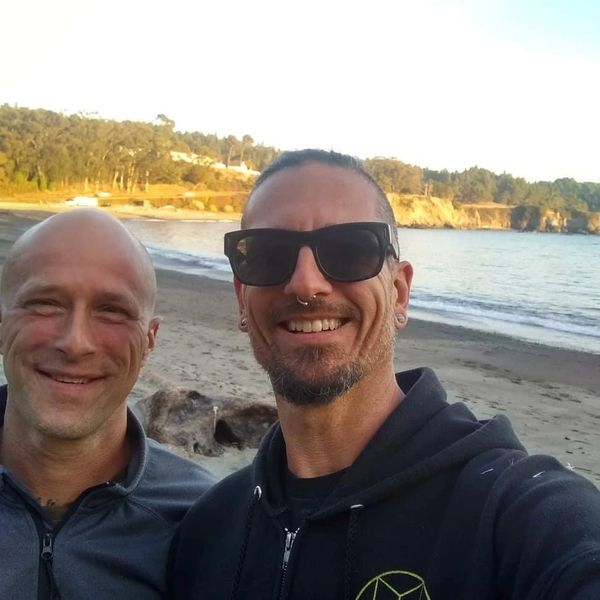 Two men smiling on a beach at sunset.