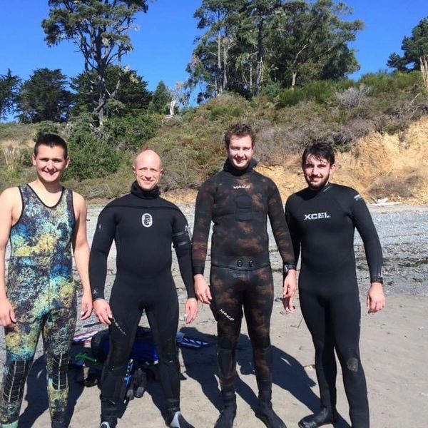 Four men in wetsuits standing on a beach.