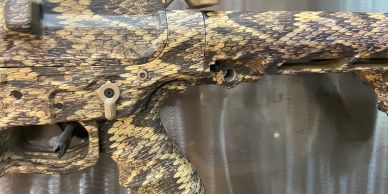 Close-up of a camouflaged rifle with a snake-skin pattern.
