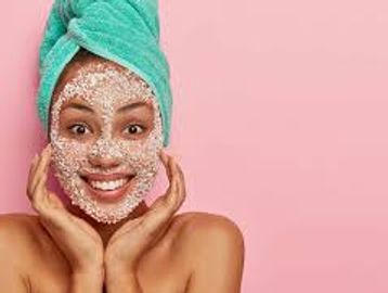 Woman with a facial scrub and a towel wrapped on her head smiling.