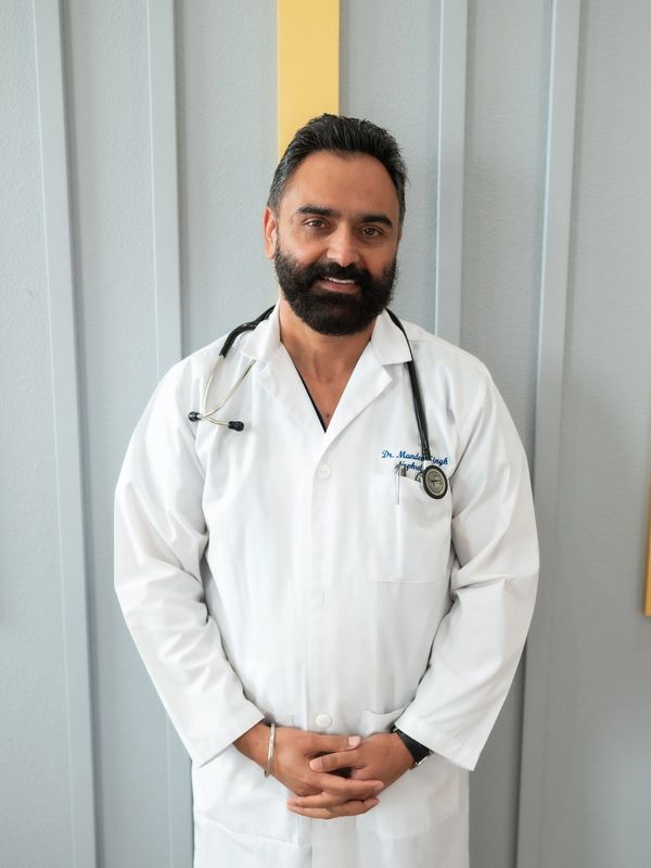 Confident doctor in white coat with stethoscope standing against a modern wall.