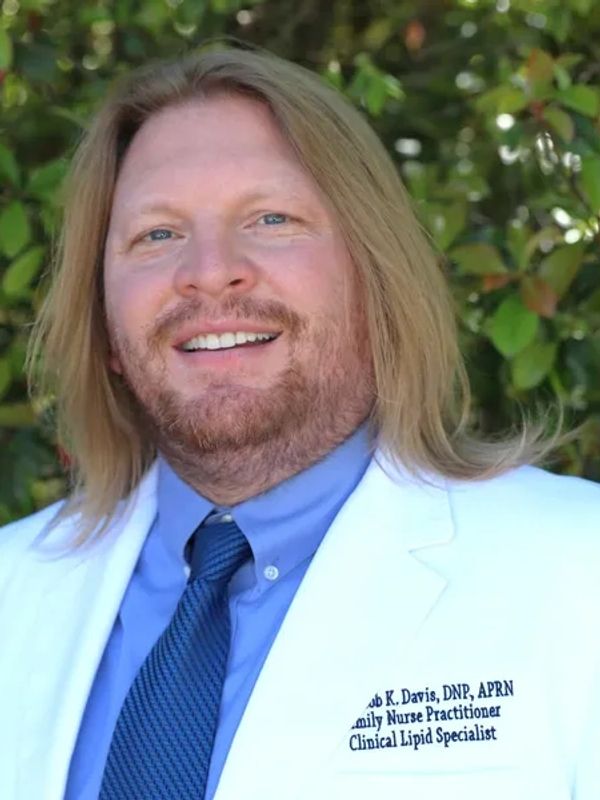 Smiling male nurse practitioner in white coat outdoors.