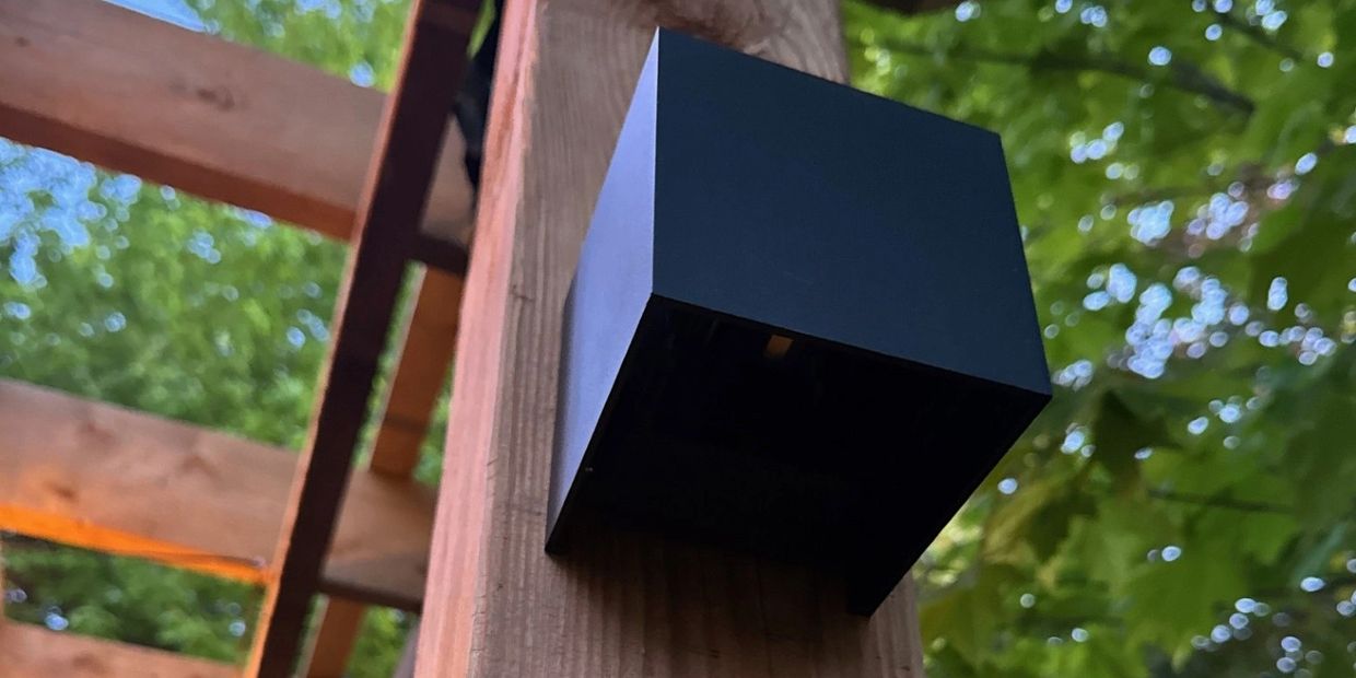 Black security camera mounted on wooden post outdoors.