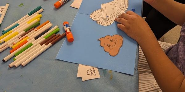 Child creating a craft with markers and glue sticks on a blue table.