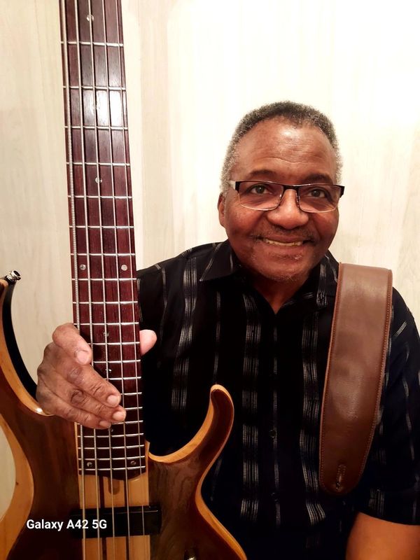 Man holding a bass guitar and smiling.