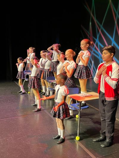 Children performing a choreographed dance on stage in school uniforms.