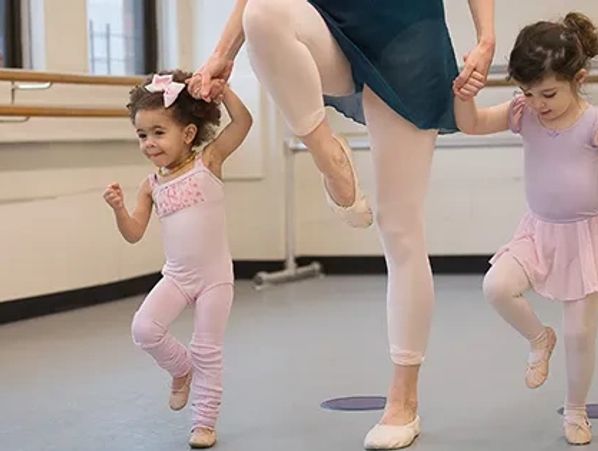 Young children in ballet class practicing with instructor.
