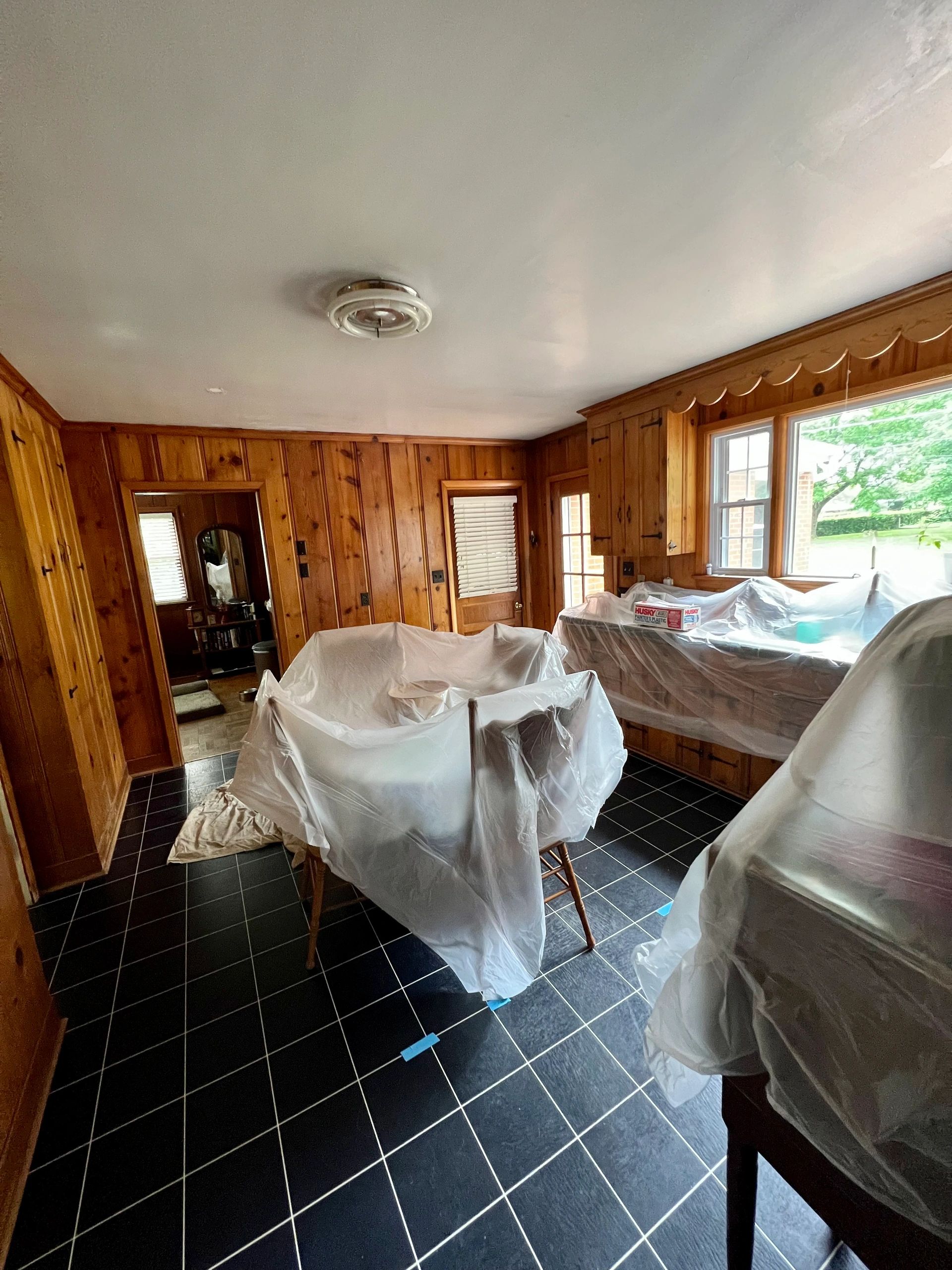 Room with wood-paneled walls and furniture covered in plastic sheets.