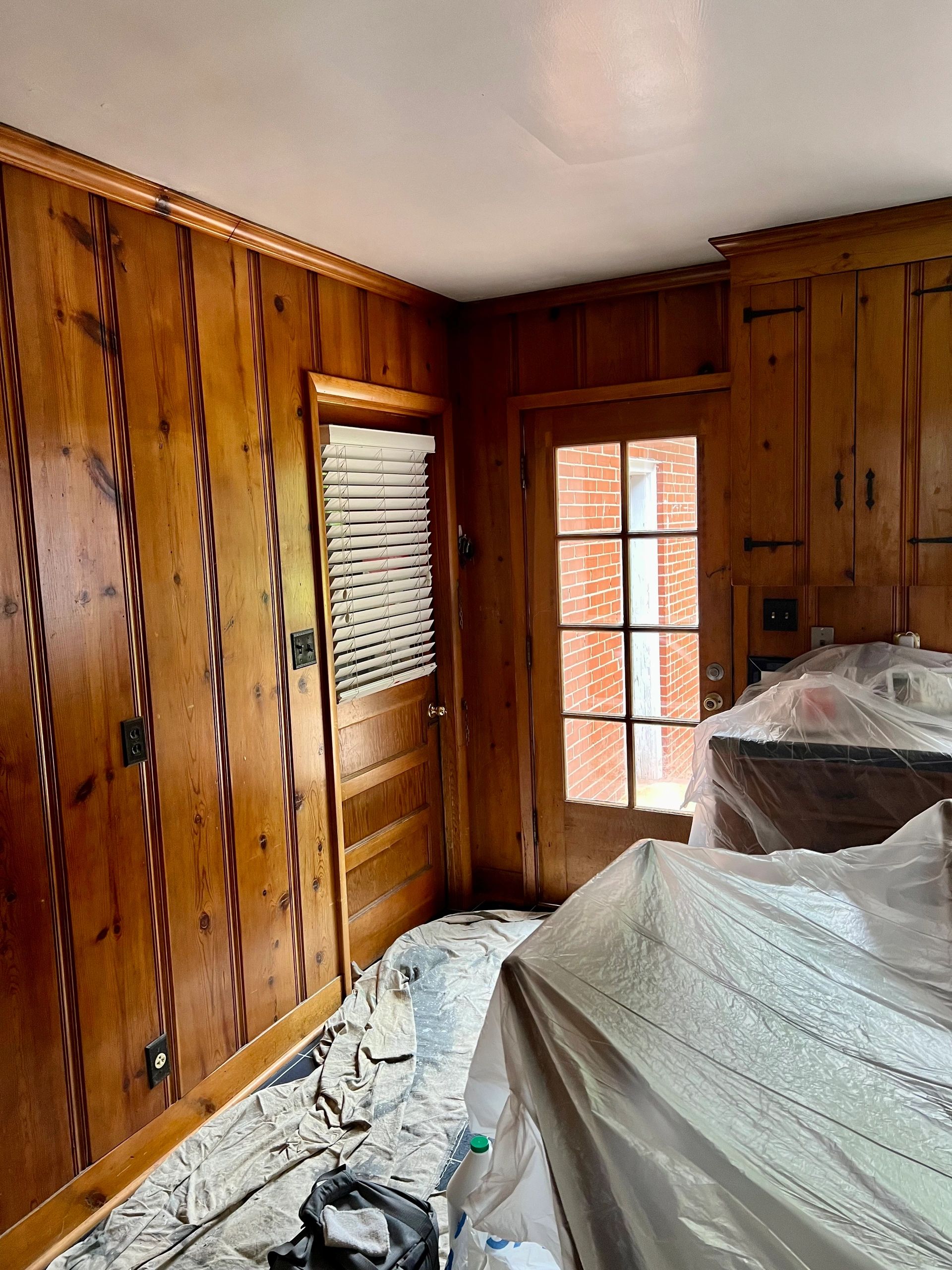 Wood-paneled room with door and covered furniture.