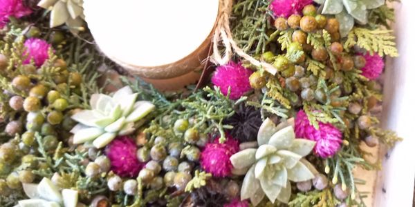 Decorative wreath with succulents, berries, and a candle in the center.