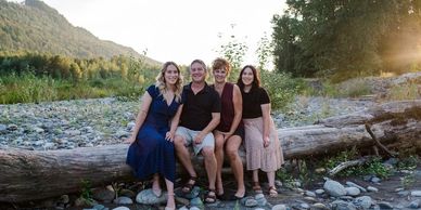 A family of four sitting on a log in a scenic outdoor setting during sunset.