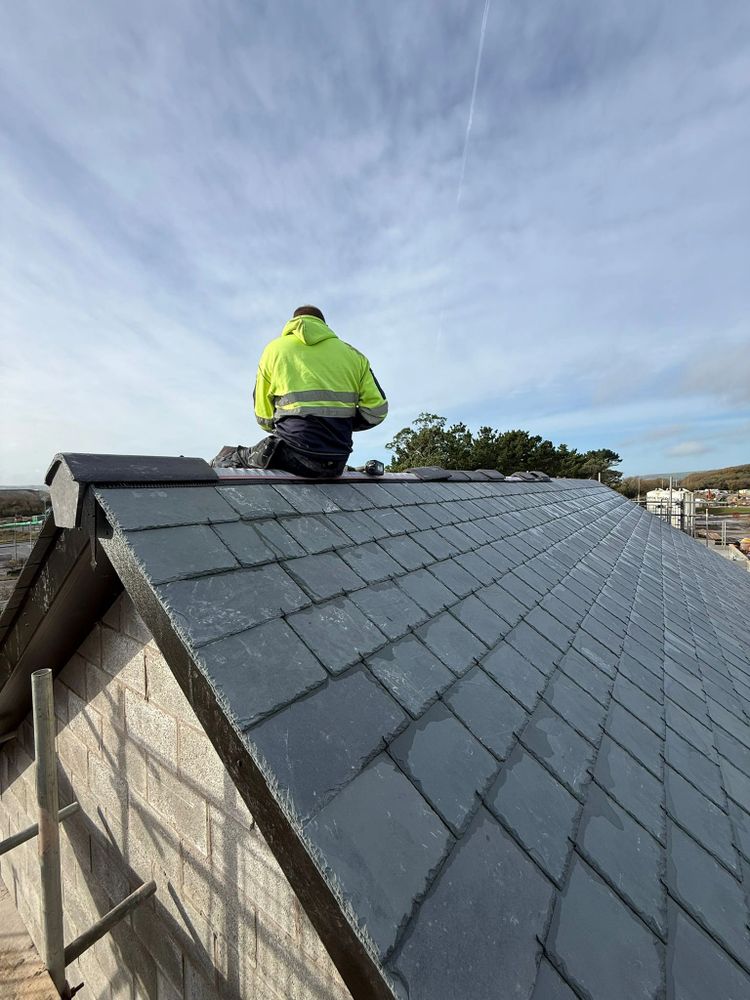 Worker in bright jacket sitting on a newly tiled slate roof.