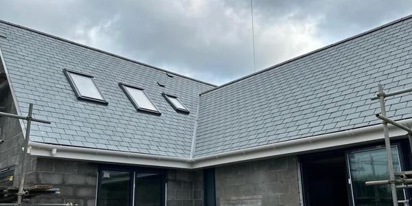 New house under construction with gray tiled roof and skylights.