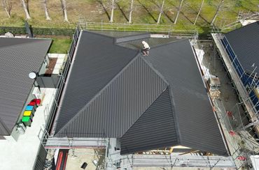 Bird's eye view looking at a person on the roof of a new house, inspecting the newly built roof.
