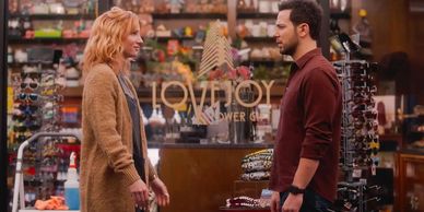 Two people have a conversation inside a shop with sunglasses displays.