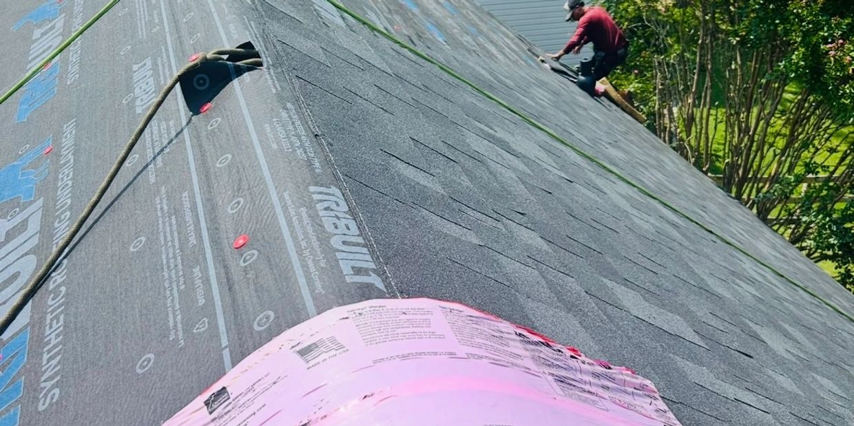 Roofing materials and a worker installing shingles on a house roof.