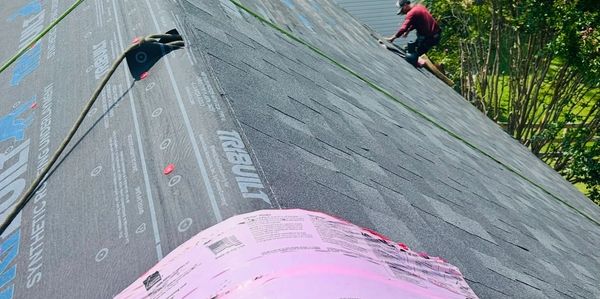 Roofing materials and a worker installing shingles on a house roof.