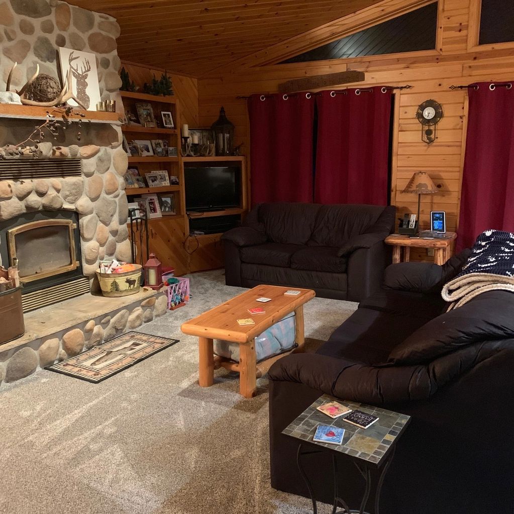 Cozy cabin living room with wooden walls and stone fireplace.
