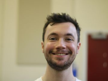 A white person with stubble and short brown hair against a slightly blurred background.