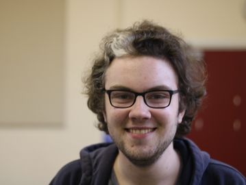 A white person with a skunk stripe and black hair smiling against a blurred background.