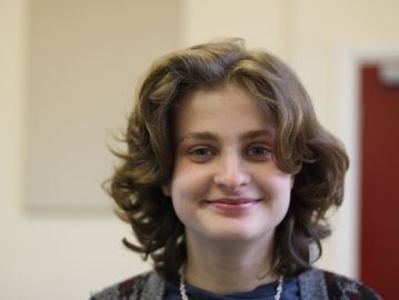 A white person with layered light brown hair smiling against a slightly blurred background.