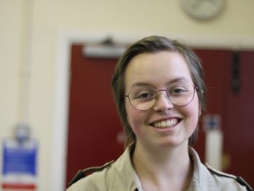 A white person with short brown hair smiling against a blurred background.