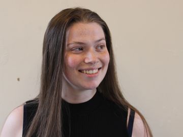 A person with long brown hair smiling at something off-camera.