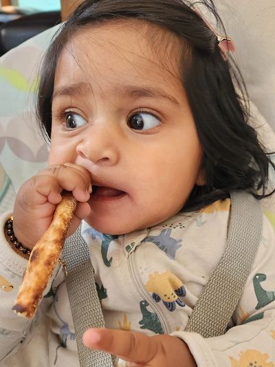 Baby eating breadstick while looking sideways.