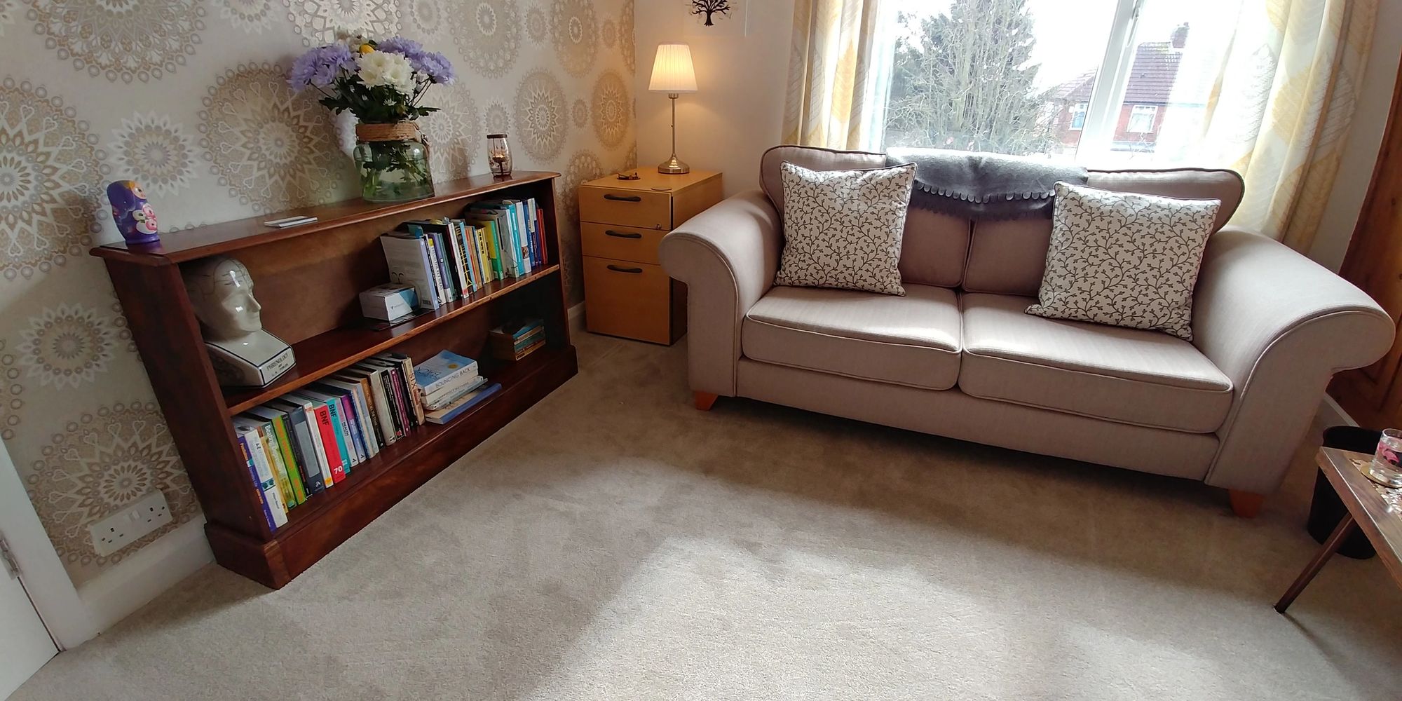 A bright airy therapy room with a light coloured sofa on the right, and a bookcase on the left. 