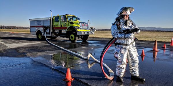 ARFF trained man holds hose in front of truck.