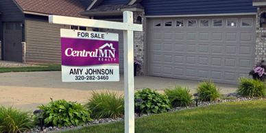Real estate for sale sign in front of a suburban house.