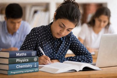 Student focused on studying with textbooks and laptop in a classroom.