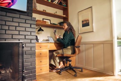 Woman working on a laptop at a wooden desk in a cozy room.
