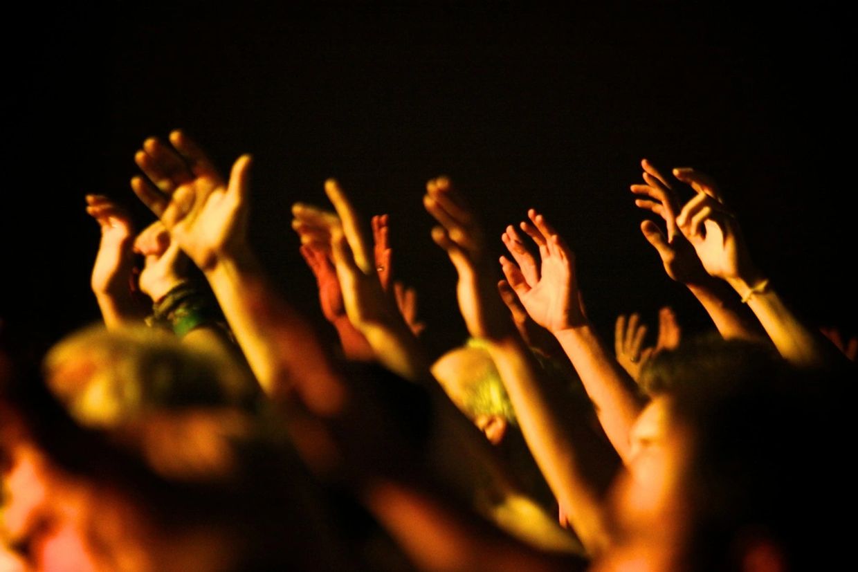 Displays worshippers from the head up, dark setting, facing light from side, heads & hands raised 