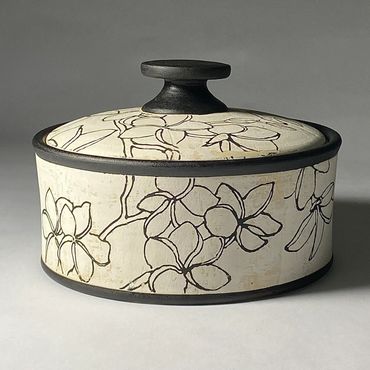 Low, wide off white ceramic jar with Plumeria flower design in black.  Black knob, rim, and base
