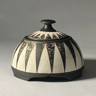 Black and white dome shaped ceramic jar with geometric design.  Raised black foot and knob.