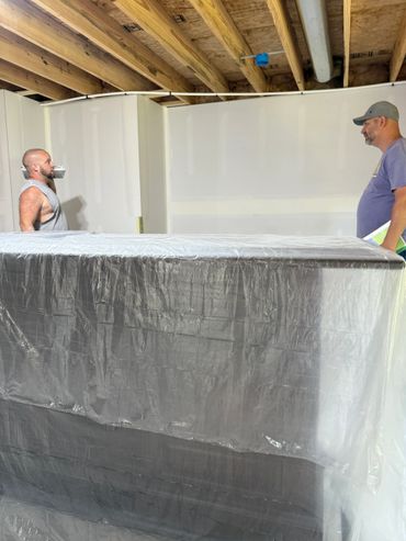 Two men standing in a room with exposed wooden ceiling beams and a covered object.