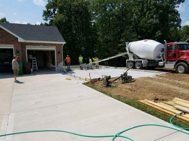 Workers pouring concrete for a driveway extension beside a brick garage.