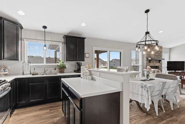Modern kitchen with dark cabinets and open dining area with chandelier.