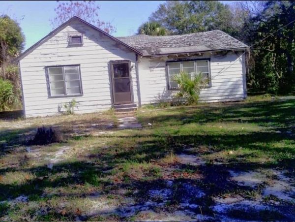 An old, weathered white house with peeling paint and a worn roof.